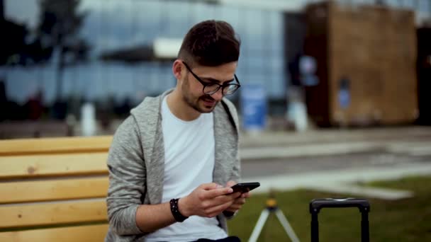 Havaalanındaki genç gezgin, elinde akıllı telefonla gülümsüyor. — Stok video