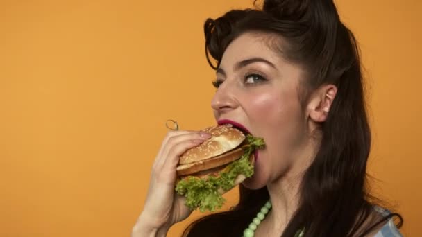 Alegre pin up chica comiendo hamburguesa y mirando a la cámara — Vídeos de Stock