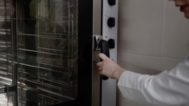 Kadın, profesyonel bir fırının kapısını açar. Metal, cam, raf, hamur işleri.
