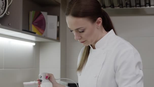Een vrouwelijke banketbakker werkt in de keuken, ze kookt, slaat iets met een blender, gefocust, druk — Stockvideo