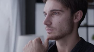 Genç bir adam pencerenin yanında duruyor, uzaklığa bakıyor, gülümsüyor ve kameraya bakıyor, ev hayatı kavramına.