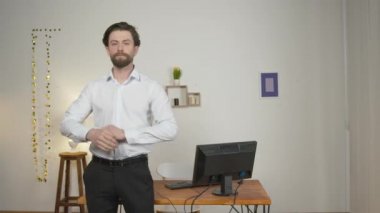 Takım elbiseli ciddi ve kendinden emin bir adam masanın yanında duruyor ve gülümsüyor.