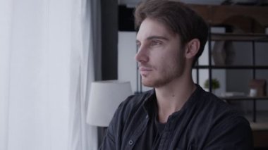 Genç bir adam pencerenin yanında duruyor, uzaklığa bakıyor, gülümsüyor ve kameraya bakıyor, ev hayatı kavramına.