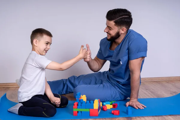 Mavi üniformalı, sakallı genç bir doktor 10 yıl boyunca çocuğun yanında oturmuş eğitici oyuncaklar oynuyorlar.