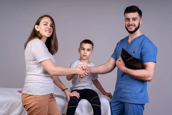 Koncepcja lekarza, syn siedzi na kanapie, a jego matka stoi obok lekarza, trzymają się za ręce. — Zdjęcie stockowe