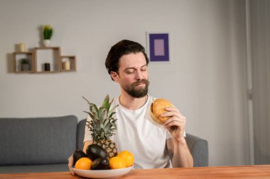 Genç bir adam masaya oturur ve meyvelerin faydasından bahseder, meyveleri toplar ve ananas, avokado, portakal gösterir. Sağlıklı yemek.