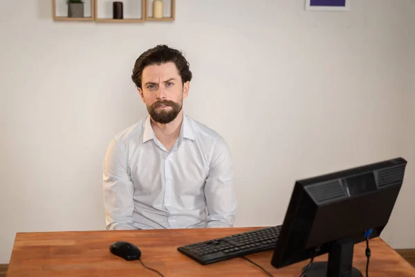 Homem trabalhador de escritório com uma barba senta-se em uma mesa com computador, um homem está cansado . — Fotografia de Stock