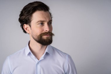 Beyaz gömlekli, sakallı genç bir adam portresi. Gülümsüyor ve başka tarafa bakıyor.