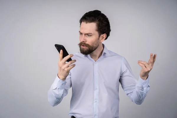 Young man with beard in white shirt emotionally talking on the phone — Stock Photo, Image