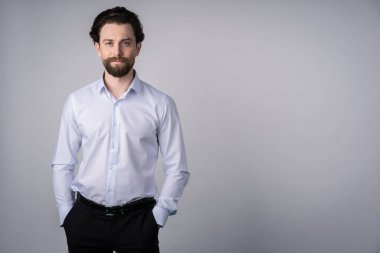 Beyaz gömlekli, sakallı, iki eli ceplerinde, kendinden emin, iş adamı gibi, ciddi bir adam.