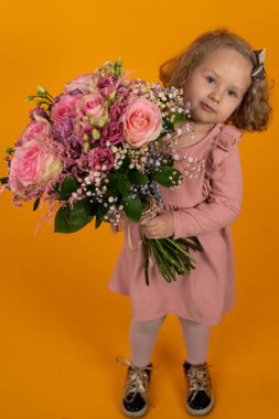 Pembe elbiseli, kıvırcık saçlı, elinde büyük bir buket pembe çiçek tutan, uzun boylu, dikey kartpostallı tatlı bir kız.
