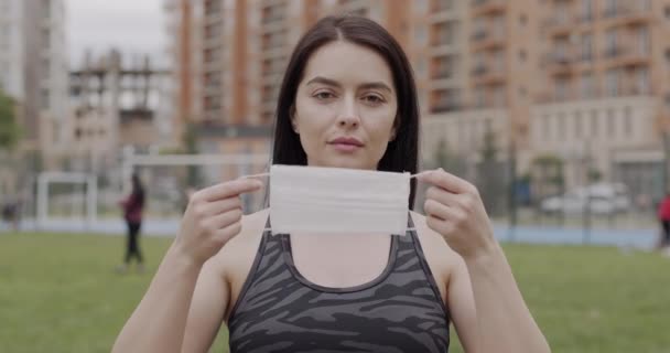 Uma menina de esportes com cabelo escuro saiu para uma pista de jogging, em movimento ela usa uma máscara médica, o conceito de proteção contra vírus e infecções — Vídeo de Stock