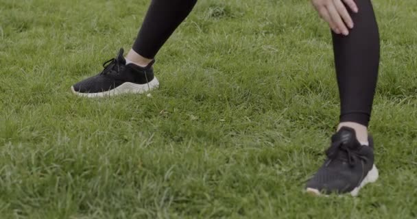 Närbild skott, flicka i svarta sneakers och leggings gör uppvärmning på gräset, begreppet hälsosam livsstil — Stockvideo