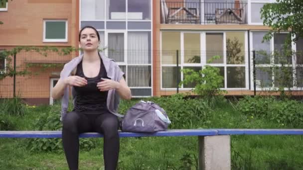 Atlétikai lány ül egy padon, majd felkel és felveszi a tornatáskáját, elmegy — Stock videók