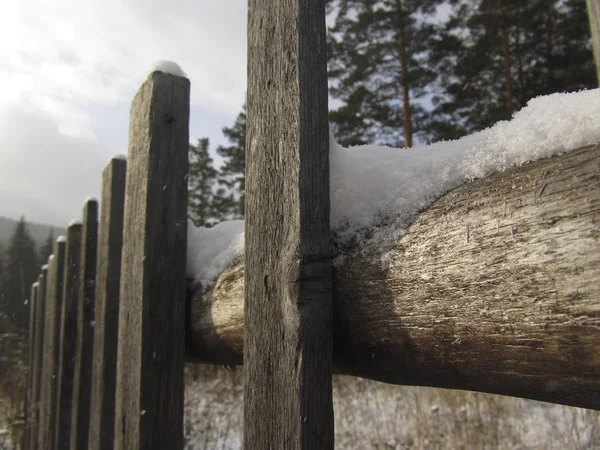 Old wooden fence in the snow. Close-up. Copy space. Winter village scene. Rural or farm fence on the background of the forest.