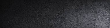 Black grunge background. Rough concrete wall texture in reflection of light closeup. Dark gray grunge banner with copy space for your design.