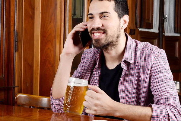 Uomo latino che parla al telefono con bicchiere di birra e snack . — Foto Stock