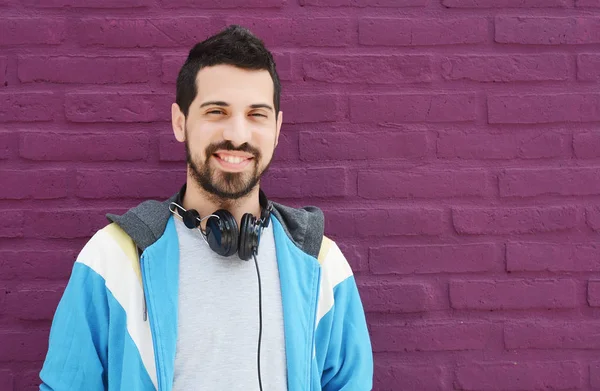 Retrato de un joven latino escuchando música con auriculares rojos contra la pared de ladrillo — Foto de Stock