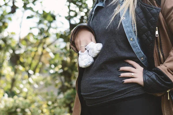 Молода вагітна жінка тримає дитячі пінетки на животі . — стокове фото