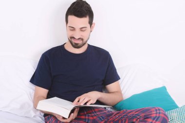 adam yatakta kitap okuma.