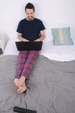 dizüstü bilgisayar kullanan yatakta adam.