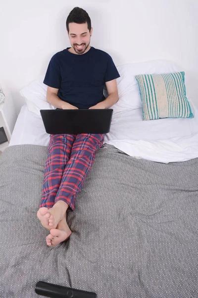 dizüstü bilgisayar kullanan yatakta adam.