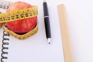 Bir elma ve not defteri üzerinde ölçüm bandı.