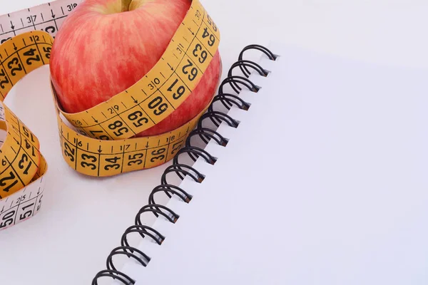 Bir elma ve not defteri üzerinde ölçüm bandı.