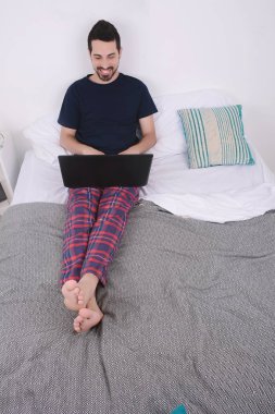 dizüstü bilgisayar kullanan yatakta adam.
