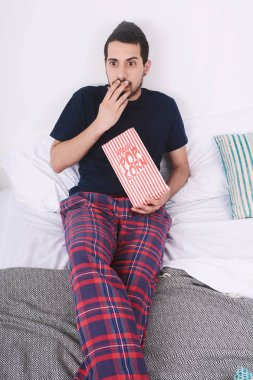 Patlamış mısır yemek ve film izlerken genç adam yatakta rahat. Kapalı.