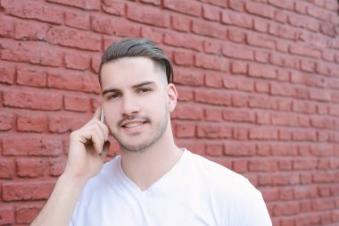 Duvara karşı telefonda konuşan genç latin adam portresi. Açık havada.