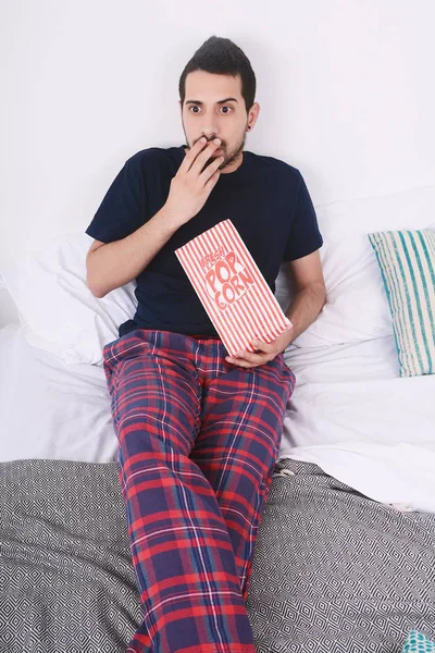 Patlamış mısır yemek ve film izlerken genç adam yatakta rahat. Kapalı.