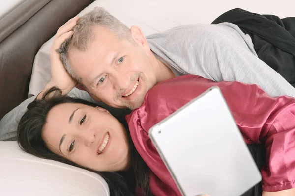 Feliz pareja de mediana edad viendo vídeo en la tableta en casa —  Fotos de Stock