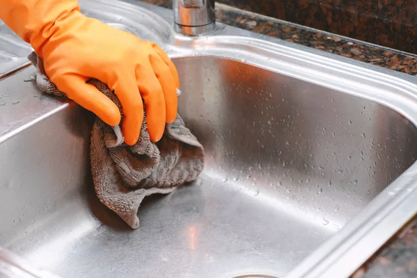 Hand with gloves wiping stainless steel sink with cloth. Housework concept
