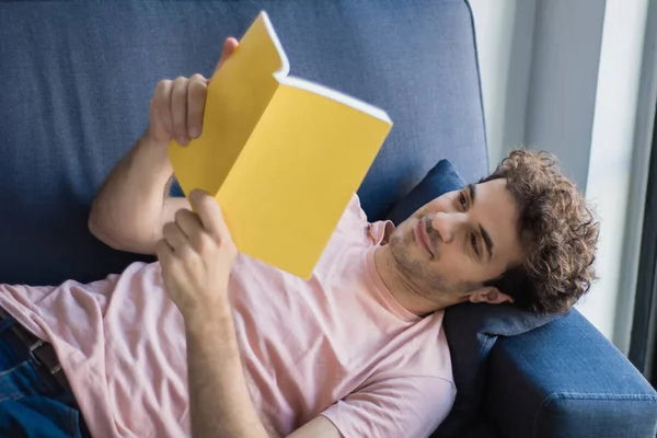 Ο άνθρωπος χαλαρά και διαβάζοντας ένα βιβλίο στον καναπέ — Φωτογραφία Αρχείου