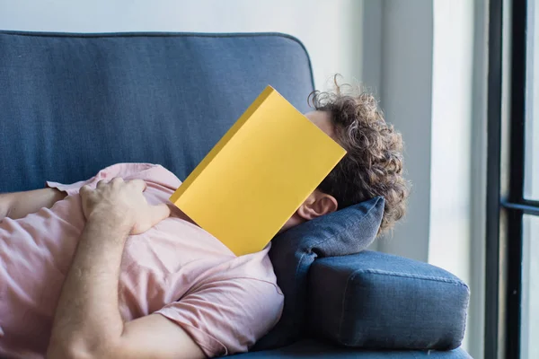 Мужчина спит на диване, прикрыв лицо книгой — стоковое фото