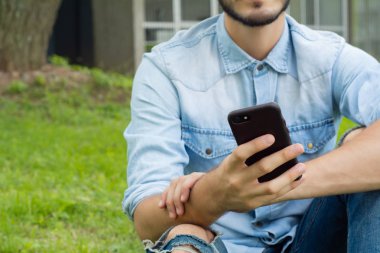 Telefonu kullanan genç bir adam. Açık havada.