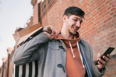 Genç adam sokakta cep telefonunu kullanıyor..