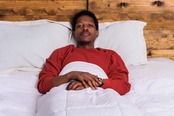 Νεαρός Αφρο άνθρωπος χαλαρώνοντας στο κρεβάτι στο σπίτι. — Φωτογραφία Αρχείου