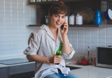 Cep telefonuyla konuşan ve bira içen bir kadın.