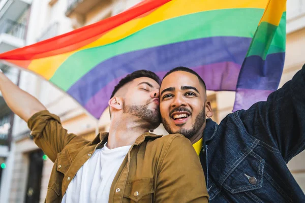 Gay pareja abrazando y mostrando su amor con arco iris bandera. —  Fotos de Stock