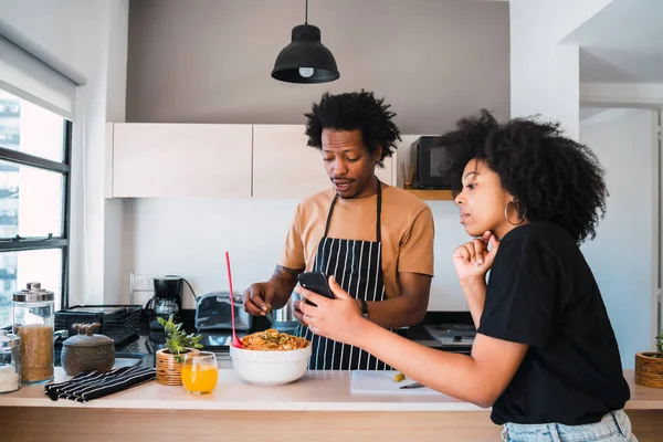 Afro pár vaření společně a pomocí telefonu doma. — Stock fotografie