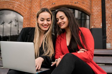 Dışarıda dizüstü bilgisayar kullanan iki genç arkadaş..