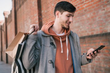 Genç adam sokakta cep telefonunu kullanıyor..