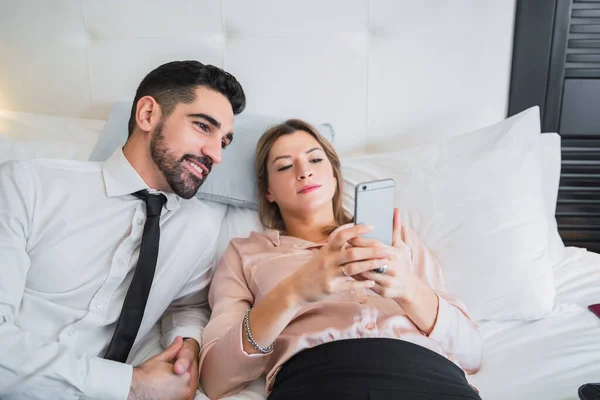 Деловые люди лежат на кровати и пользуются мобильным телефоном. — стоковое фото