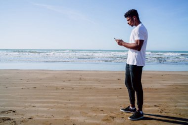 Sahilde antremana ara verdiğinde cep telefonunu kullanan bir atletin portresi. Spor ve sağlık yaşam tarzı.