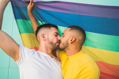 Sokakta gökkuşağı bayrağıyla kucaklaşan ve sevgilerini gösteren genç eşcinsel çiftin portresi. LGBT ve aşk konsepti