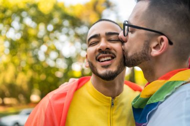Genç eşcinsel çiftin portresi. Sokakta gökkuşağı bayrağıyla kucaklaşıp sevgilerini gösteriyorlar. LGBT ve aşk konsepti