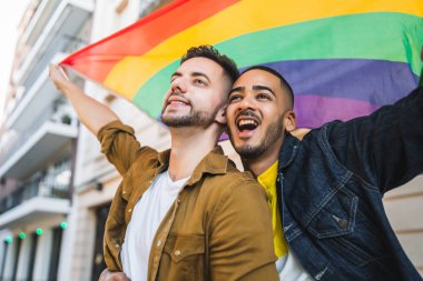 Sokakta gökkuşağı bayrağıyla kucaklaşan ve sevgilerini gösteren genç eşcinsel çiftin portresi. LGBT ve aşk konsepti
