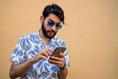 Sarı arka planda cep telefonunu kullanan genç Latin adamın portresi. İletişim konsepti.